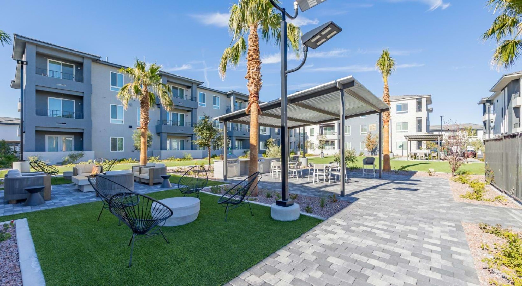 An outdoor apartment courtyard featuring palm trees, artificial turf with seating, and a covered grilling area.