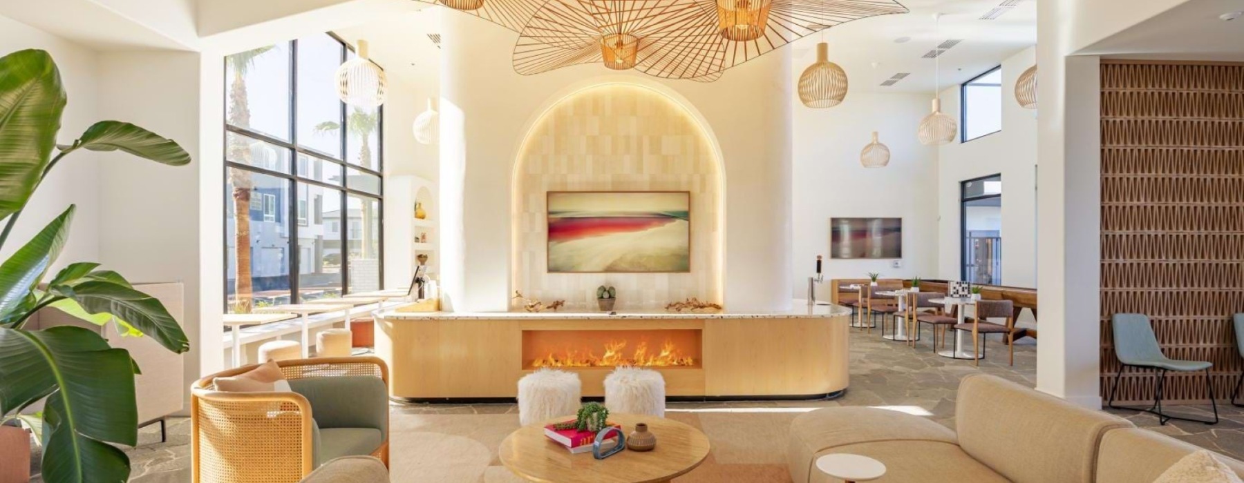 A spacious apartment lounge featuring modern furniture, a linear fireplace, and decorative light fixtures hanging above.