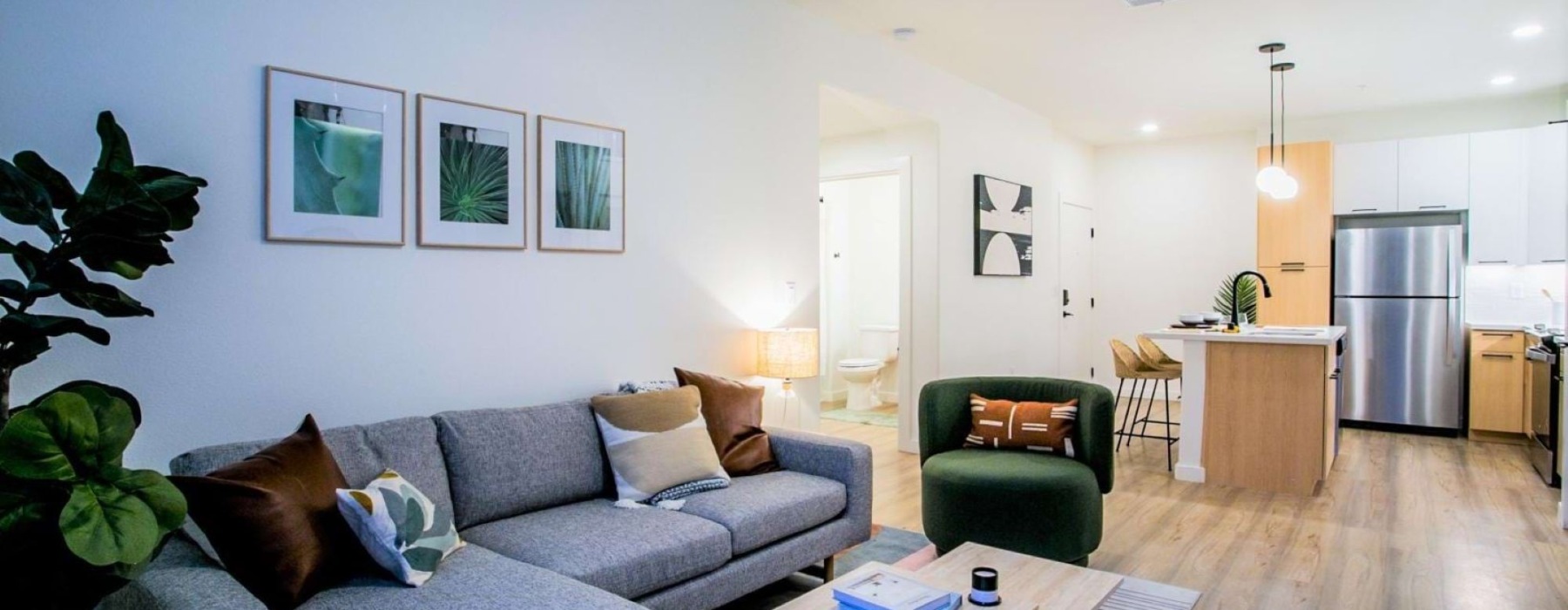 An open-concept apartment living area showing a grey sectional couch, green armchair, and kitchen island.