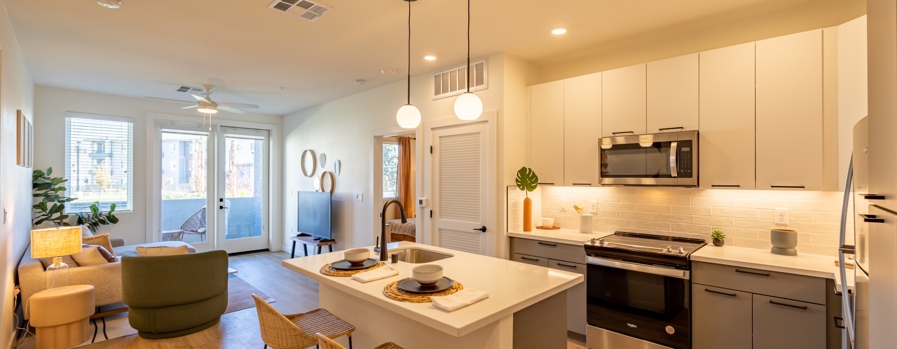 An open-concept apartment kitchen and  living area showing a grey sectional couch, green armchair, and kitchen island.