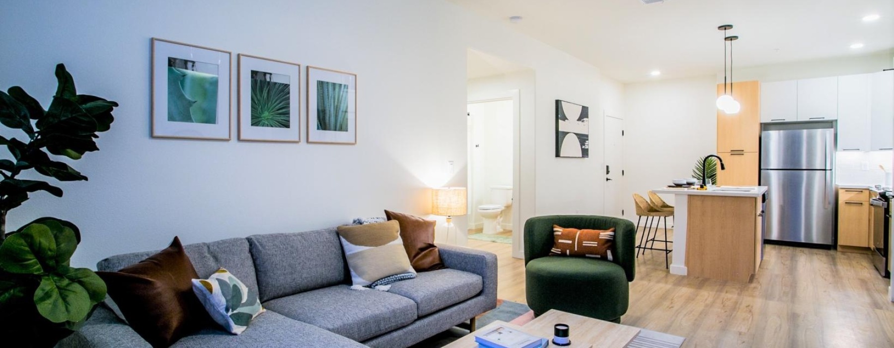 A bright, light-filled apartment living room with a couch and side table — the kind of open, well-lit space that can double as a work-from-home zone.